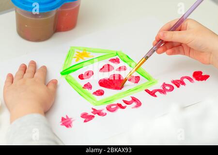 Kind zeichnet Herz im Haus auf weißem Blatt Papier mit Worten bleiben zu Hause. Stay Home Konzept. Kreativität für Kinder. Stockfoto