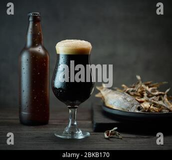 Dunkles Bierglas und Flasche sowie gesalzene getrocknete Fischgerichte Stockfoto