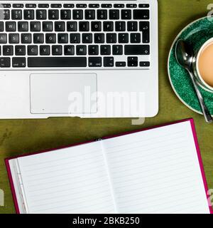 Freiberufliche Remote-Arbeitsstation, Nahaufnahme EINES Laptops ohne Personen und EINE Tasse Tee oder Kaffee mit einem offenen Notizbuch Stockfoto