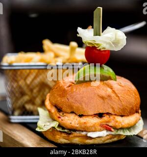 Frisch gekochter würziger Chicken Burger in EINEM gerösteten Brötchen mit EINEM Korb mit Chips oder Pommes Frites, ohne Leute Stockfoto