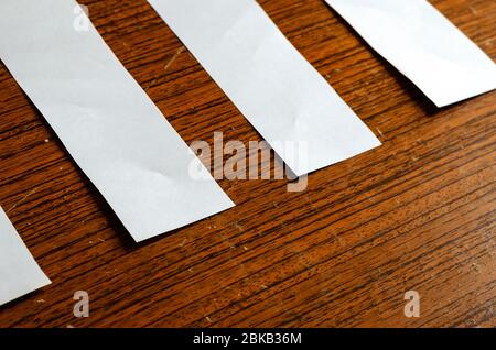 Streifen aus weißem Papier auf einer alten Informationstafel. Leere Papierblätter auf braunem Holzhintergrund. Kreativer Hintergrund mit Kratzern und Kratzern. Trainieren Stockfoto