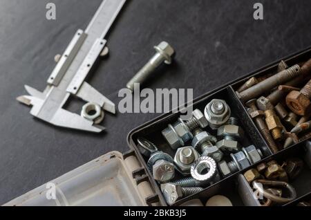 Bremssattel und Kasten mit Schrauben und Muttern. Die Wahl des richtigen Metallverbinders. Verwendung von manuellen Messgeräten. Fokus im Vordergrund. Nahaufnahme. Stockfoto