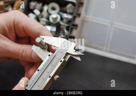 Eine männliche Hand mit einem Bremssattel misst den Durchmesser einer Schraube. Die Wahl des richtigen Metallverbinders. Verwendung von manuellen Messgeräten. Fokus in der Stirn Stockfoto