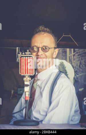 Retro, Porträt Nahaufnahme des Mannes aus den 1940er Jahren als Sprecher am Vintage-Mikrofon, Severn Valley Heritage Railway 1940er WWII Sommerveranstaltung, Großbritannien. Stockfoto