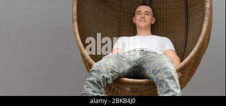 Schöner Mann sitzt auf Korbsessel im Freien Stockfoto