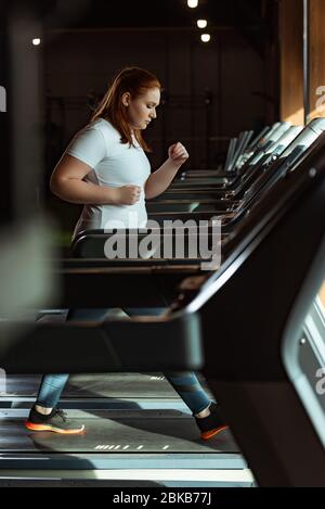 Selektive Konzentration von konzentrierten übergewichtigen Mädchen läuft auf dem Laufband im Fitnessstudio Stockfoto