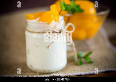 Hausgemachter süßer Joghurt mit Scheiben eingelegter Pfirsiche in einem Glasgefäß Stockfoto