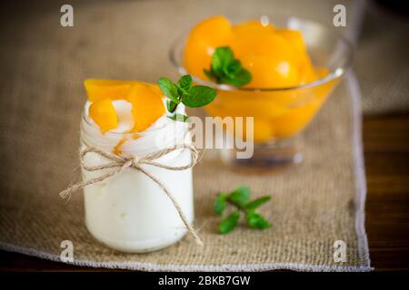 Hausgemachter süßer Joghurt mit Scheiben eingelegter Pfirsiche in einem Glasgefäß Stockfoto