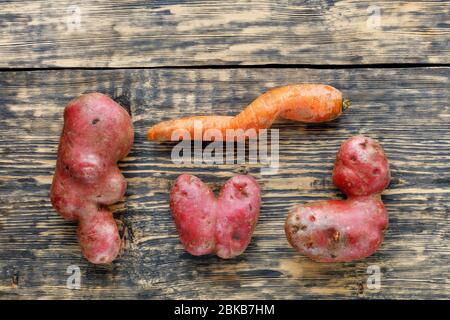 Hässliches lustiges Gemüse, herzförmige Kartoffeln und verdrehte Karotte auf einem gestreiften braunen Holzhintergrund. Das Konzept der grobkörmigen Gemüse oder Lebensmittelabfälle. Stockfoto