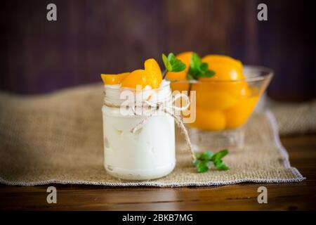 Hausgemachter süßer Joghurt mit Scheiben eingelegter Pfirsiche in einem Glasgefäß Stockfoto
