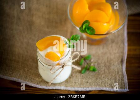 Hausgemachter süßer Joghurt mit Scheiben eingelegter Pfirsiche in einem Glasgefäß Stockfoto
