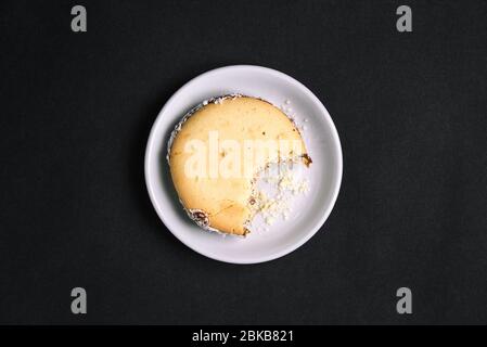 Das gebissene Plätzchen befindet sich auf einer weißen Platte. Süßes Gebäck und Krümel. Draufsicht auf schwarzem Hintergrund. Flaches Layout Stockfoto