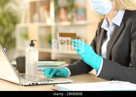 Nahaufnahme der Unternehmerin, die online mit Kreditkarte auf Laptop zahlt, um Coronavirus mit Maske und Handschuhen zu vermeiden, die im Homeoffice sitzen Stockfoto