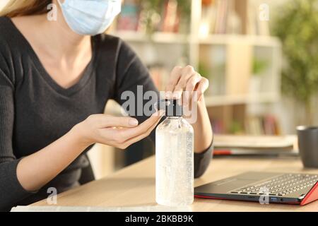 Nahaufnahme der Frau, die Coronavirus vermeiden Handdesinfektionsmittel aus dem Flaschenspender auf einem Schreibtisch zu Hause sitzen Stockfoto