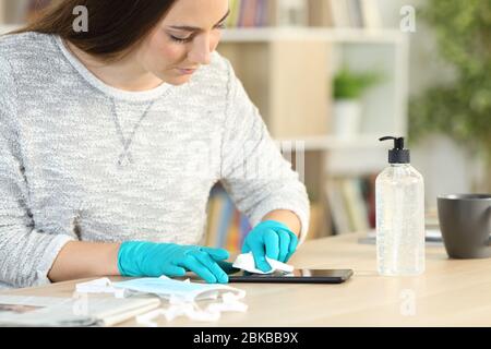 Frau desinfizieren Smartphone-Bildschirm mit Desinfektionsmittel Gel Vermeidung von Coronavirus mit Latexhandschuhe zu Hause Stockfoto