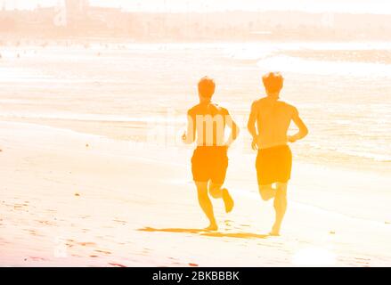 Zwei Männer laufen auf Sand in der Nähe von Meer, Meer, Wasser bei Sonnenuntergang, Menschen laufen am Strand, Silhouetten von Läufern Stockfoto