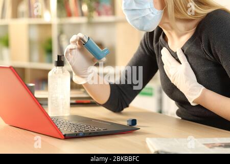 Asthmatische Frau hält Inhalator erstickt mit Coronavirus Symptome sitzen auf einem Schreibtisch zu Hause Stockfoto