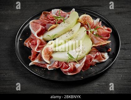 Teller mit Melone und Schinken auf schwarzem Holztisch Stockfoto