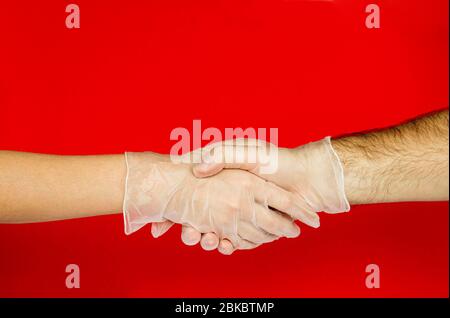 Handschütteln Männer und Frauen Hand in medizinischen Handschuhen auf rotem Hintergrund. COVID-19.Coronavirus. Stockfoto