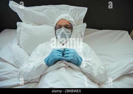 Mann in Gefahrgutanzug, medizinische Maske und Brille im Schlafzimmer schlafen Stockfoto