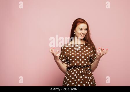 Das rothaarige Mädchen ist überrascht und schockiert. Frau erlebt eine Emotion der Wut auf einem rosa Hintergrund im Studio. Stockfoto