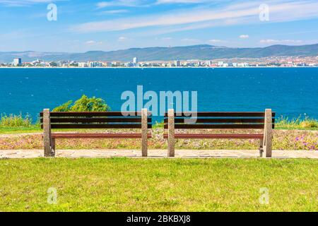 Zwei Bänke am sonnigen Strand. Schöne Skyline Blick aus leeren Park mit gepflasterten Fußweg am Meer. Stadt und Berg in der Ferne ben Stockfoto