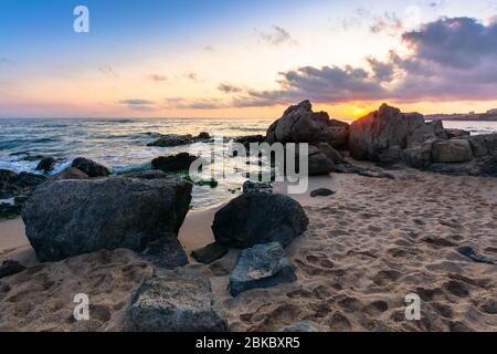 Dramatischer Sonnenaufgang am Meer. Wellen schlagen Felsen am Sandstrand. Schöne Wolkenlandschaft über dem Horizont Stockfoto