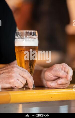 Ein großes Glas Bier auf einer Holzbar und eine Männerhand, ganz nah Stockfoto