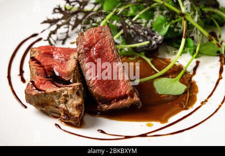 Mittelgroßes, rares Rindfleisch mit Salat und Sauce aus grünen Blättern. Nahaufnahme. Stockfoto