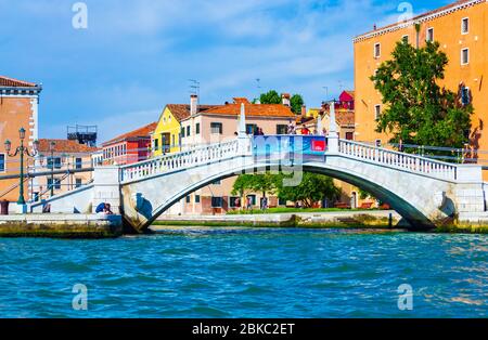 Historische Gebäude entlang der Uferpromenade und der Fußgängerbrücke von Puente Arsenale über den Kanal Rio dell Arsenale, von einem Boot aus gesehen Lagune von Venedig blaues Wasser Stockfoto