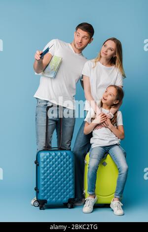 Eltern und Tochter schockierten mit Reisetaschen, Karte und Pässen auf blau Stockfoto