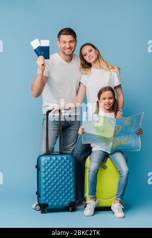 Lächelnde Eltern und Tochter mit Reisetaschen, Karte, Tickets und Pässen auf blau Stockfoto