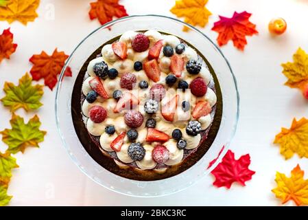 Köstliche Tarte mit frischen Erdbeeren, Himbeeren und Johannisbeeren auf dem Tisch. Draufsicht horizontal. Vor dem Hintergrund der Herbstblätter Stockfoto