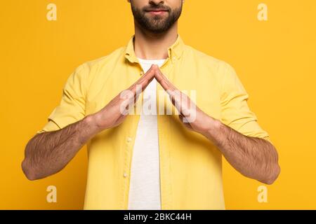 Zugeschnittene Ansicht des Mannes, der Hauszeichen in tauber und stummer Sprache auf gelbem Hintergrund zeigt Stockfoto
