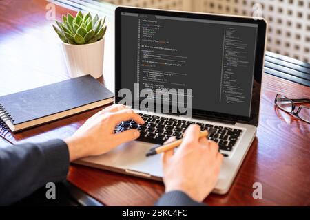 Computercode, Softwarekonzept. Programmierer, die mit einem Laptop arbeiten, Programmiercode auf dem Bildschirm, Bürohintergrund. Entwicklung von Codierungstechnologien. Stockfoto