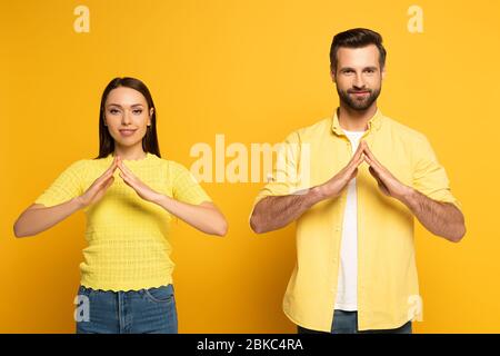 Junges lächelndes Paar zeigt Geste nach Hause in Gebärdensprache auf gelbem Hintergrund Stockfoto