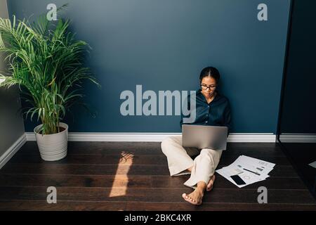 Blick aus dem Hochwinkel auf die Geschäftsfrau, die im Wohnzimmer auf dem Boden sitzt. Junge Frau, die ihr Online-Geschäft von zu Hause aus verwaltet. Stockfoto