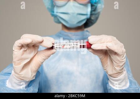 Cropped Ansicht des Arztes, der Reagenzglas mit Blutprobe und Coronavirus Schriftzug auf grau isoliert hält Stockfoto