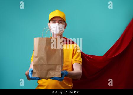 Kurier mit Tasche trägt medizinische Gesichtsmaske in Superhelden Mantel. Konzept der Superheldentum Kurier während Coronavirus Ausbruch. Stockfoto