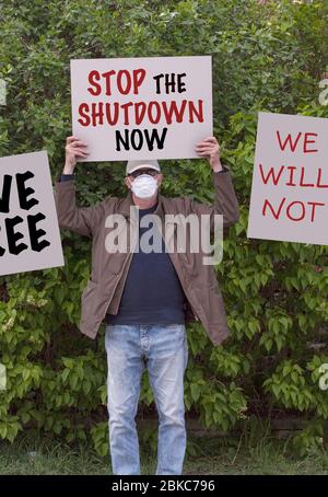 Protester mit Kappe und medizinischer Schutzmaske demonstrieren gegen Verbleib bei Hausbestellungen aufgrund der COVID-19-Pandemie mit dem Schild Stop the Shutdown Stockfoto