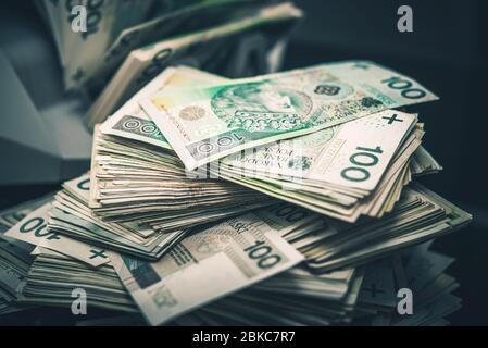 Riesiger Haufen polnischer Zloty Cash Money auf einem Tisch. Geldscheinzählmaschine im Hintergrund. Finanzindustrie. Stockfoto