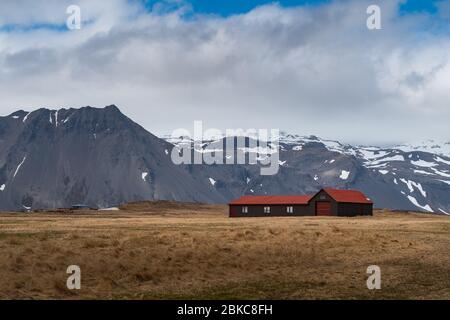 Abgelegenes Haus in einer dramatischen Landschaft isländischer typischer Natur mit hohen und scharfen Bergen und langen flachen Ländern. Schöne Landschaft von Island Stockfoto