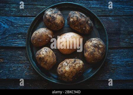 Schmutzige und gewaschen junge rohe Kartoffeln in einem Teller auf einem hölzernen alten Tisch Bio-Lebensmittel Stockfoto