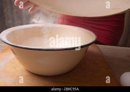 Große Schüssel, Schneidebrett, Sieb zum Sieben von Mehl auf dem Tisch. Weibliche Hände sieben Mehl in der Küche. Stockfoto