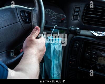 Kaukasischer Mann fährt ein Auto, schützende medizinische Masken hängen an der Schaltung eines Automatikgetriebes, das er anlegt, wenn er nach draußen geht Stockfoto