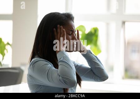 Unglückliche afroamerikanische Geschäftsfrau, die an Kopfschmerzen bei der Arbeit leidet. Stockfoto