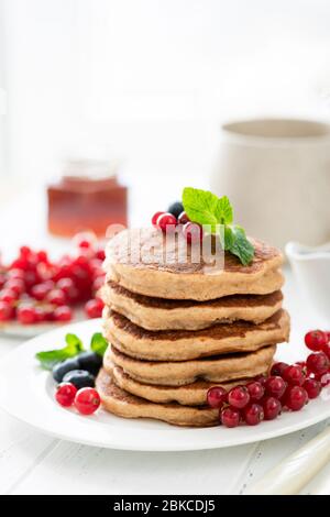 Stapel von leckeren Pfannkuchen mit Beeren auf weißem Tisch gekrönt. Frühstück, flauschige amerikanische Buttermilch-Pfannkuchen Stockfoto