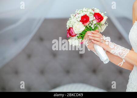 Elegante Frau Braut sanft hält ein Bouquet von Blumen und Rosen mit ihren zarten Händen. Hochzeitstag im Schlafzimmer Haus. Stockfoto