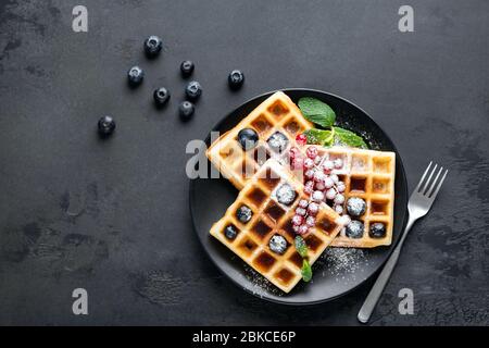 Quadratische belgische Waffeln mit Beeren und Puderzucker auf schwarzem Teller, schwarzer Hintergrund mit Kopierfläche. Table Top Blick Zucker Dessert auf dem Teller Stockfoto