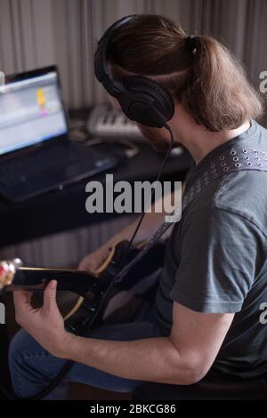 Bärtiger Mann Musiker Musik spielen und komponieren ein Lied mit E-Gitarre Klavier und Laptop-Computer, während im Wohnzimmer sitzen, Corona Virus quar Stockfoto